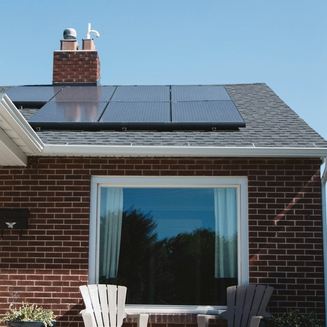 Vivint Solar - Solar Panels on roof of brick home with window and Adirondack chairs.